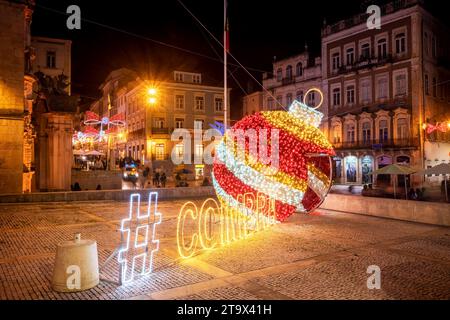 Coimbra, Portogallo - 21 novembre 2023: Bright Christmas Ball e Coimbra hashtag con gli edifici di piazza 8 de Maio sullo sfondo, di notte. Foto Stock