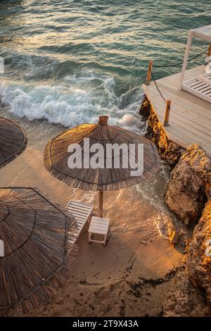 Paesaggio verticale di Sandy Beach con ombrello di paglia e onde del Mar Ionio. Spiaggia di Ksamil, nell'Albania meridionale. Foto Stock