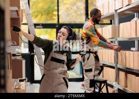 Storehouse Manager che esegue la scansione dei dettagli delle scatole di cartone utilizzando lo scanner del punto vendita, esaminando l'elenco di controllo durante l'inventario delle stanze di stoccaggio. Il supervisore prepara i pacchetti dei clienti che lavorano al processo di spedizione Foto Stock