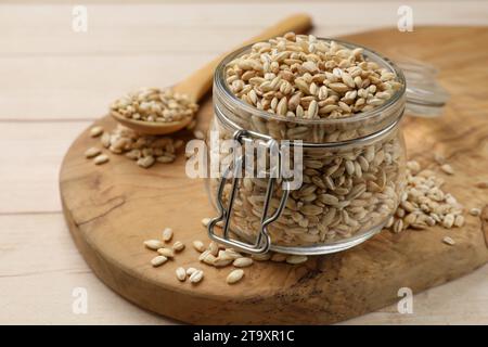 Asciugare l'orzo perlato in vaso di vetro e cucchiaio su un tavolo di legno chiaro, primo piano Foto Stock