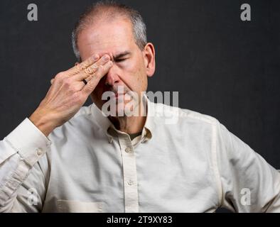 Un uomo di 60 anni tiene il lato della testa in disagio Foto Stock