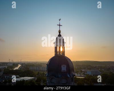 Un'eterea alba offre uno sfondo maestoso alla silhouette di una cupola della chiesa, la sua croce luccicante mentre cattura la prima luce. La cupola, simbolo di spiritualità e di grandezza architettonica, sorge sopra il paesaggio urbano circostante, offrendo un momento di riflessione e di pace. Mentre la giornata si rompe, il cielo passa dalle arance calde al blu tenue, annunciando un nuovo giorno con un senso di speranza e rinnovamento. Divine Dawn: La cupola della chiesa si staglia contro l'alba. Foto di alta qualità Foto Stock