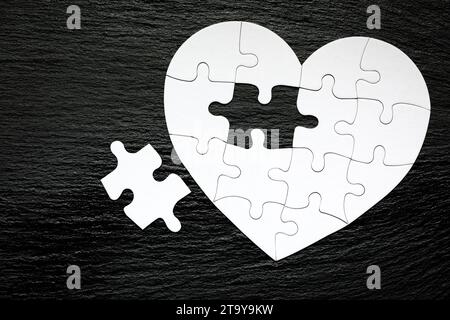 A forma di cuore puzzle sul colore di sfondo. Puzzle cuore su sfondo di legno. Un pezzo mancante del puzzle di cuore. Forma di cuore puzzle. Puz Foto Stock