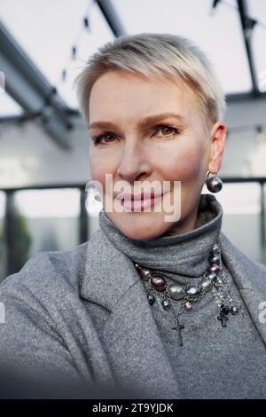 Selfie di bella donna bionda matura con taglio corto. Ritratto ravvicinato di un elegante modello femminile di mezza età con occhi marroni che guardano la videocamera Foto Stock