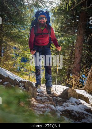 Un uomo barbuto con uno zaino che fa escursioni in montagna in inverno. Bel tempo in una giornata invernale di sole in montagna Foto Stock