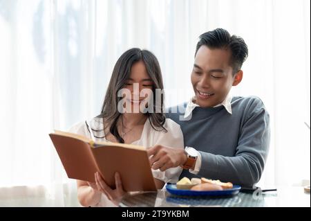 Giovane, bella e adorabile coppia asiatica che condivide il tempo libero insieme, leggendo libri in un grazioso caffè. Concetto di coppia. Foto Stock