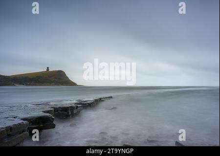 La luce svanisce sulla spiaggia rocciosa di Kimmeridge Bay sulla costa meridionale dell'Inghilterra, in una giornata nuvolosa. La Clavell Tower può essere vista sul promontorio. Foto Stock