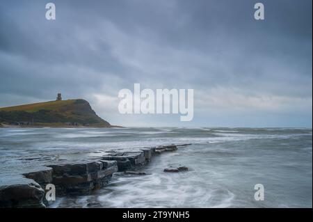 La luce svanisce sulla spiaggia rocciosa di Kimmeridge Bay sulla costa meridionale dell'Inghilterra, in una giornata nuvolosa. La Clavell Tower può essere vista sul promontorio. Foto Stock