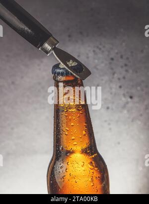 bottiglia di birra fresca fresca fredda con gocce e tappo aperto con apribottiglie su sfondo scuro Foto Stock
