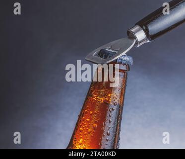 bottiglia di birra fresca fresca fredda con gocce e tappo aperto con apribottiglie su sfondo scuro Foto Stock