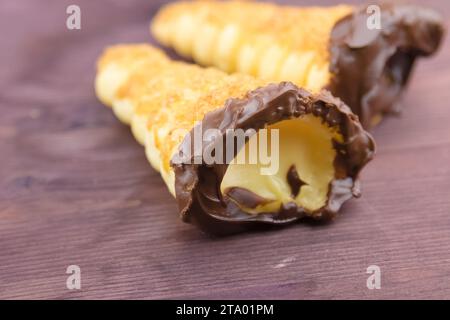 delizioso cannolo siciliano cannellino dolce con pasticceria cioccolato alle nocciole e crema pasticcera, pasta sfoglia italiana su fondo di legno, concetto nutrizionale e dietetico Foto Stock