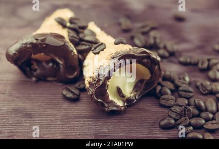 delizioso cannolo siciliano cannellino dolce con pasticceria cioccolato alla nocciola e crema pasticcera vicino ai chicchi di caffè, pasta sfoglia italiana su fondo di legno, concetto nutrizionale e dietetico Foto Stock