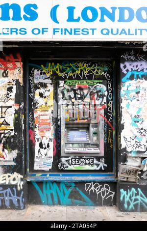 Bancomat o bancomat integrati nel muro di un edificio. Il bancomat è sul lato della strada. E' in servizio ma e' completamente coperto di graffiti e adesivi Foto Stock