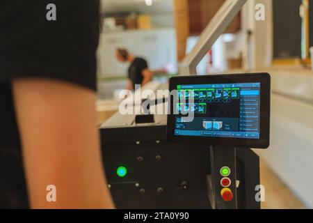 Pannello di controllo touchscreen di macchinari con lavoratori in background in un'officina Foto Stock