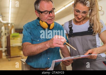 uomo e donna che esaminano un documento in un laboratorio di falegnameria Foto Stock