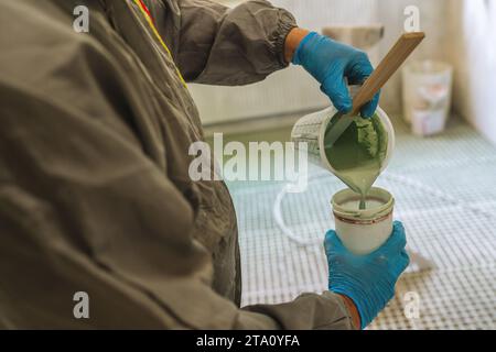 persona che indossa un dispositivo di protezione versando vernice verde in una lattina Foto Stock
