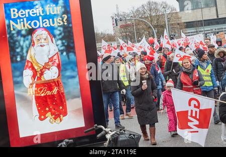 Amburgo, Germania. 28 novembre 2023. I dimostranti con bandiere GEW camminano davanti a un cartellone con un motivo di Babbo Natale al cioccolato durante una manifestazione su Stephansplatz. L'Education and Science Union (GEW) aveva invitato tutti i dipendenti del settore pubblico negli stati federali a partecipare al primo giorno di sciopero dell'istruzione a livello nazionale. Crediti: Georg Wendt/dpa/Alamy Live News Foto Stock