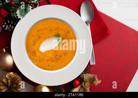 Crema di carote e zucca con panna e noci. Cibo natalizio servito su un tavolo decorato con motivi natalizi. Foto Stock