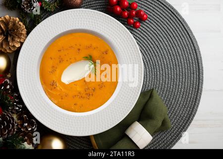 Crema di carote e zucca con panna e noci. Cibo natalizio servito su un tavolo decorato con motivi natalizi. Foto Stock