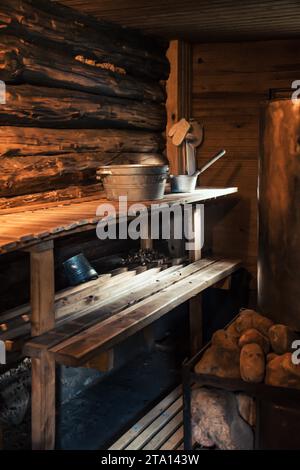 Interno di una tradizionale sauna in legno con secchio e mestolo in metallo posti su una panca in legno. Atmosfera accogliente e rustica tipica della Scandinavia, del Baltico Foto Stock