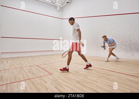 uomini attivi e diversi in abbigliamento sportivo che giocano a squash in campo, sfida e motivazione Foto Stock