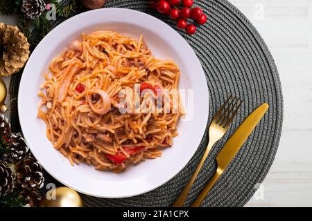 Fideua con calamari e frutti di mare. Tipica tapa spagnola cotta con paella. Cibo natalizio servito su un tavolo decorato con motivi natalizi. Foto Stock