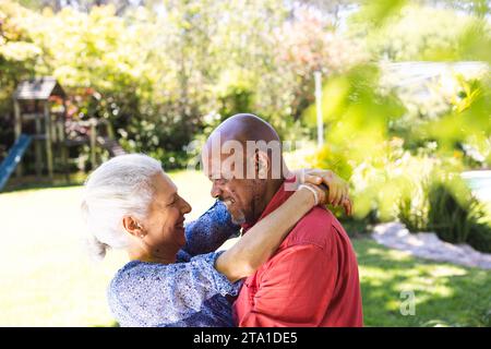 Coppia anziana felice e diversificata che si abbraccia in un giardino soleggiato. Stile di vita, pensione, stile di vita anziano, natura, insieme e vita domestica, inalterati. Foto Stock