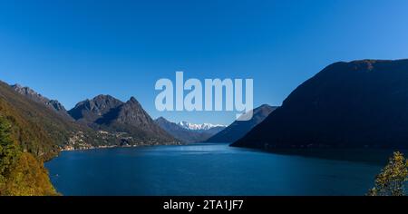Una vista panoramica del Lago di Lugano con verdi colline e cime innevate sotto un cielo blu Foto Stock