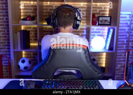 Uomo di mezza età con la barba che gioca ai videogiochi e indossa cuffie in piedi all'indietro guardando lontano con le braccia incrociate Foto Stock