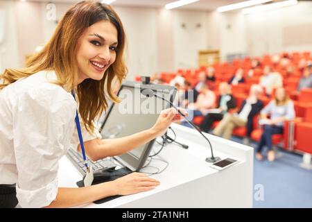 Ritratto di una sorridente oratrice che tiene la parola tramite microfono sul podio durante il seminario presso il centro congressi Foto Stock