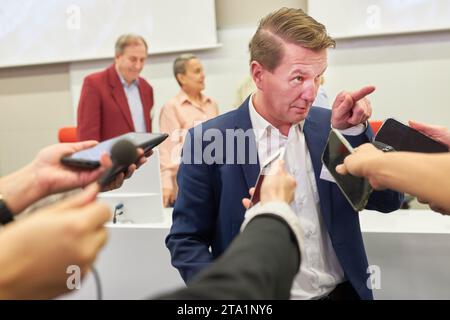 Altoparlante uomo d'affari che punta mentre parla con i giornalisti con microfoni e telefoni alla conferenza stampa Foto Stock