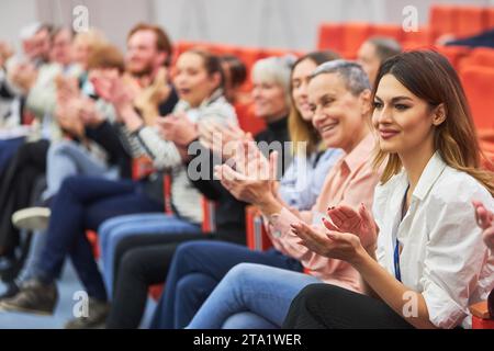 Professionisti maschili e femminili che battono le mani mentre si siedono in udienza a una conferenza d'affari nell'auditorium Foto Stock