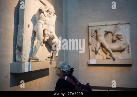 I visitatori del British Museum di Londra ammireranno le metope del Partenone greco antico, conosciute anche come i marmi del Partenone (Elgin), il 28 novembre 2023, a Londra, in Inghilterra. Novantadue metope erano lastre di marmo rettangolari poste sopra le colonne del tempio del Partenone di Atene raffiguranti scene della mitologia greca. Foto Stock