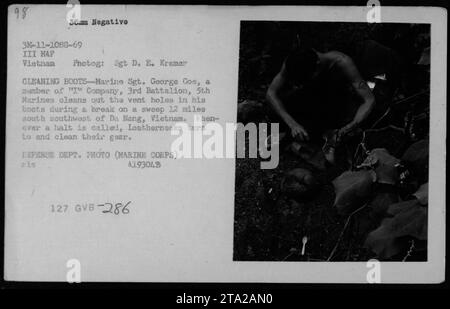 George Coe, della compagnia "i", 3rd Battalion, 5th Marines, è raffigurato mentre pulisce i fori di sfiato nei suoi stivali durante una pausa durante una missione di sweep a 12 miglia a sud-ovest di da Nang, Vietnam. Era pratica comune per i Marines pulire la loro attrezzatura durante i fermi. Foto Stock