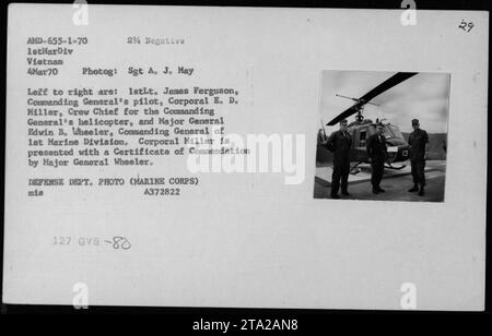 Il maggiore generale Edwin B. Wheeler, comandante generale della 1st Marine Division in Vietnam, presenta il caporale E. D. Miller, il capo dell'equipaggio dell'elicottero del Comandante generale, con un certificato di Commendazione. 1stLT. James Ferguson, pilota del comandante generale, è presente anche durante la cerimonia. Fotografia scattata il 4 marzo 1970. Foto Stock