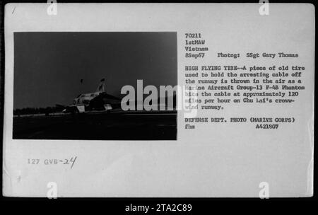 "Marine Aircraft Group-13 F-4 Phantom colpisce il cavo di arresto a circa 120 km/h sulla pista ad ala di corvo di Chu Lai durante la guerra del Vietnam. Un pezzo di vecchio pneumatico utilizzato per trattenere il cavo dalla pista viene gettato nell'aria. Fotografia scattata l'8 settembre 1967 da SSgt Gary Thomas. Dipartimento difesa Foto (corpo dei Marines)." Foto Stock