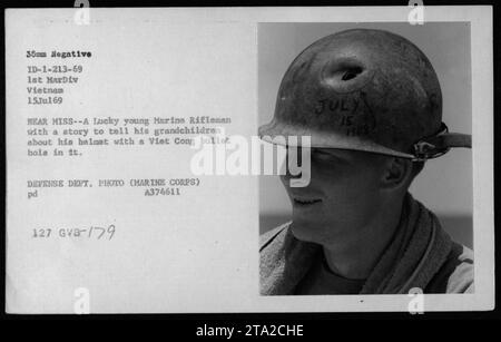 Un Marine degli Stati Uniti della 1st Marine Division nella guerra del Vietnam mostra il suo casco perforato da un proiettile di un Viet Cong vicino a Miss. Questa foto, scattata il 15 luglio 1969, cattura la fortunata sopravvivenza del marine e serve come promemoria dell'intensità dei combattimenti durante il conflitto. Foto Stock