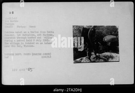 Un Marine della Delta Company, 1st Battalion, 4th Marines, cerca un villaggio bombardato su un'isola vicino a Cho Lai, in Vietnam, il 9 luglio 1965. I nativi guardano mentre le attività militari americane continuano durante la guerra del Vietnam. Questa fotografia è stata scattata da Gorak e fa parte della collezione del Dipartimento della difesa. (Didascalia: Un Marine cerca un villaggio bombardato durante una pattuglia vicino a Cho Lai, Vietnam nel luglio 1965.) Foto Stock