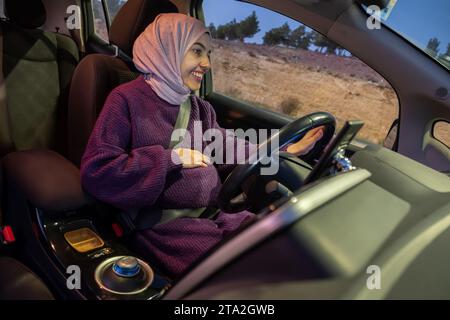 Donna musulmana araba incinta che guida un'auto di notte indossando abiti invernali, hijab e cintura di sicurezza, guidando in modo sicuro e sicuro Foto Stock
