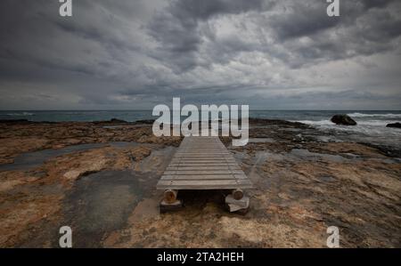 Onde tempestose cielo nuvoloso molo vuoto di legno su una costa rocciosa Foto Stock