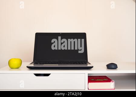 Computer portatile vuoto aperto con mockup e schermo nero su tavolo da scrivania bianco. Mela gialla e topo. Libro. Area di lavoro moderna Foto Stock