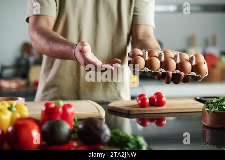 Primo piano di un uomo irriconoscibile che tiene una scatola di uova sopra il tavolo della cucina Foto Stock