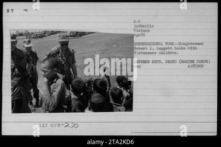 Il deputato Robert L. Leggett si impegna in una conversazione con i bambini vietnamiti durante un tour congressuale in Vietnam nell'aprile 1966. Questa foto cattura ufficiali e funzionari coinvolti in attività militari durante la guerra del Vietnam, tra cui il presidente Lyndon Johnson e il colonnello P X Kelley. Foto Stock