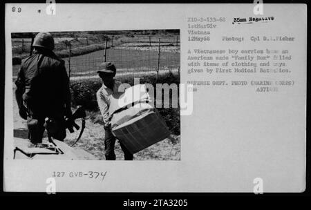 Civili vietnamiti che ricevono aiuti dal primo Battaglione medico durante la guerra del Vietnam. Un ragazzo porta con sé una "Family Box" di fabbricazione americana piena di vestiti e provviste fornite dal battaglione. Questa fotografia, scattata il 12 maggio 1968, descrive gli sforzi compiuti dall'esercito statunitense per aiutare le comunità locali durante il conflitto. Foto Stock