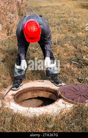 L'idraulico ha aperto il portello del pozzo e si è appoggiato sopra di esso. Manutenzione di serbatoi e pozzi settici nelle zone rurali. Foto Stock