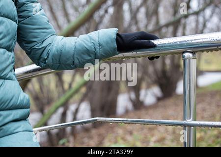 donna che si aggrappa alle ringhiere di metallo mentre sale le scale in caso di pioggia. tenere la mano su un corrimano metallico coperto da gocce di pioggia. Foto Stock