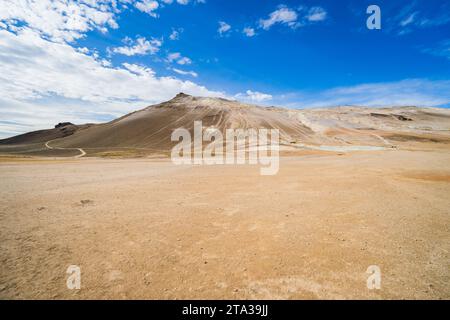 Un tratto solitario di strada sterrata si snoda attraverso una valle soleggiata, passando attraverso un paesaggio desolato e arido Foto Stock