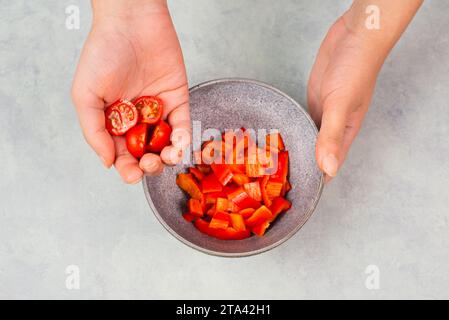 Pomodori e peperoni rossi a fette in una ciotola, preparare cibo sano con verdure di paprika, tenendo in mano la nutrizione biologica fresca Foto Stock