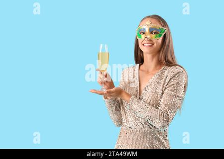 Bellissima giovane donna in maschera carnevalesca con un bicchiere di champagne su sfondo blu Foto Stock