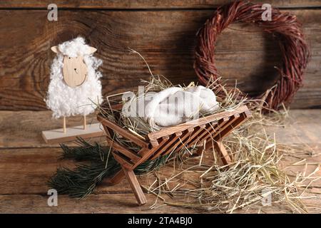 Manger con manichino di bambino e pecora su sfondo di legno. Concetto di storia di Natale Foto Stock